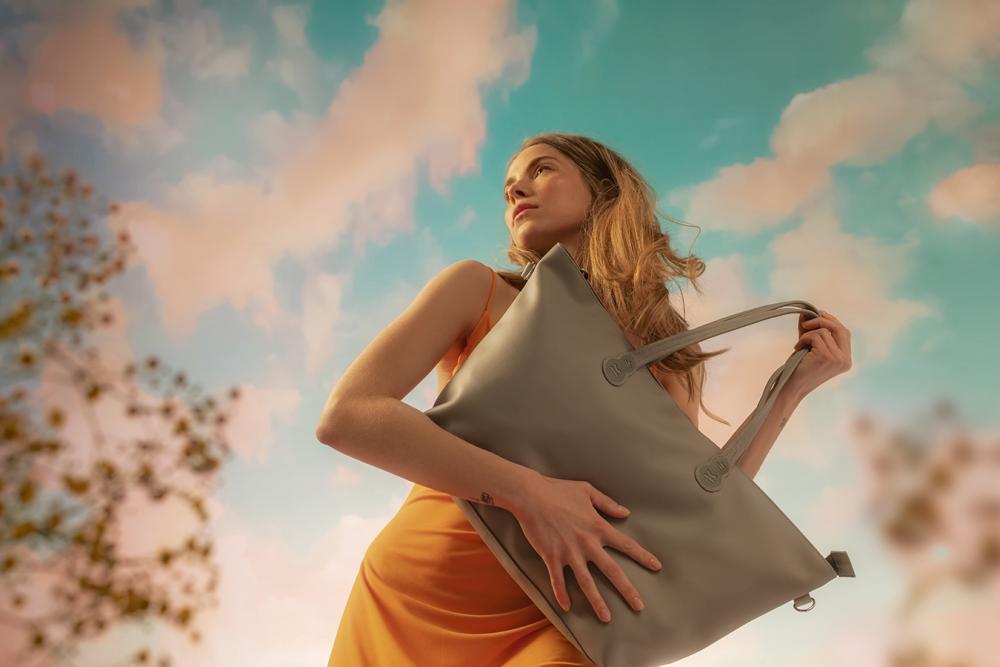 Donna con in mano una borsa della collezione Nature Vibes , donna in piedi su uno sfondo di nuvole