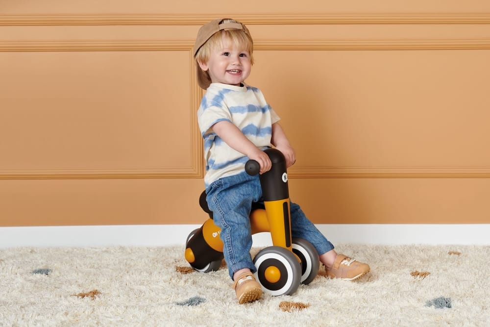 Un ragazzino sorridente e felice con in testa un berretto da baseball è seduto su una bicicletta MINIBI gialla