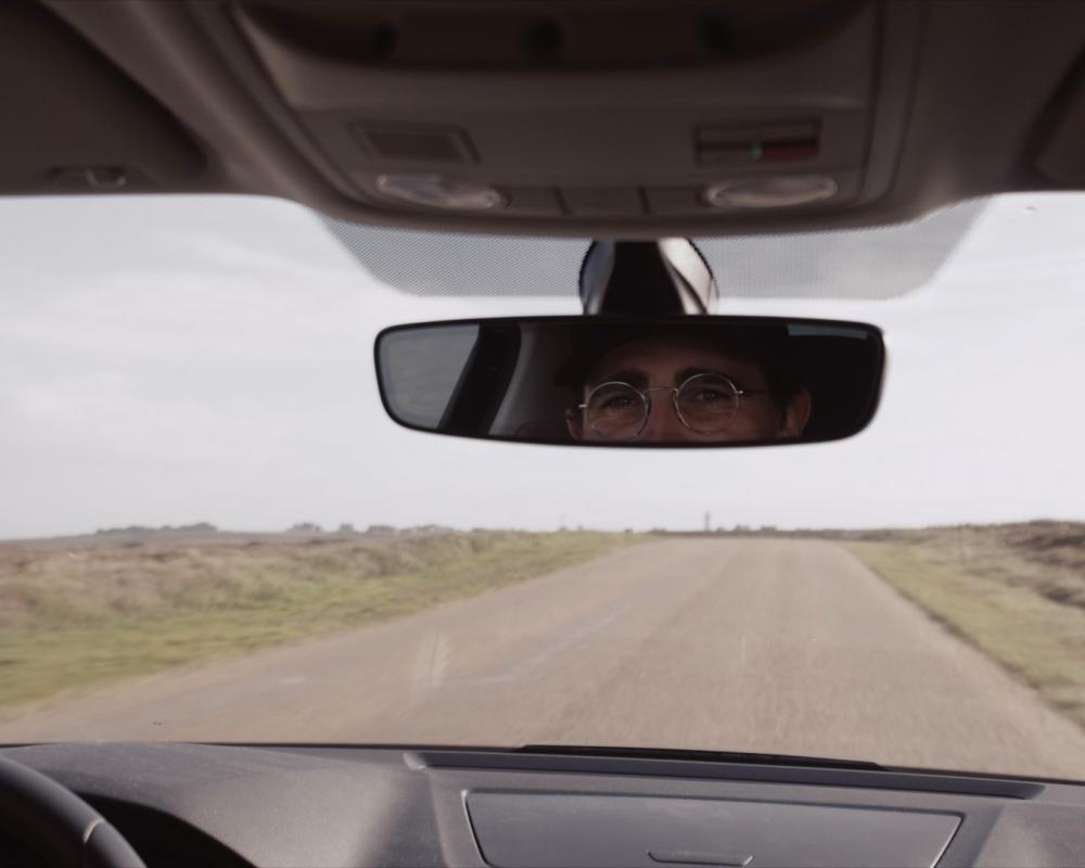 Vista attraverso il parabrezza durante la guida con la rifflessione del guidatore nello specchietto frontale.