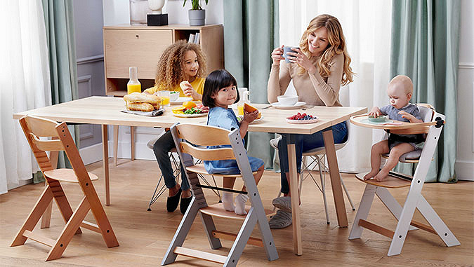 La mamma e tre bambini stanno facendo colazione seduti a tavola. Due bambini più piccoli stanno seduti sui seggiolini di Kinderkraft.