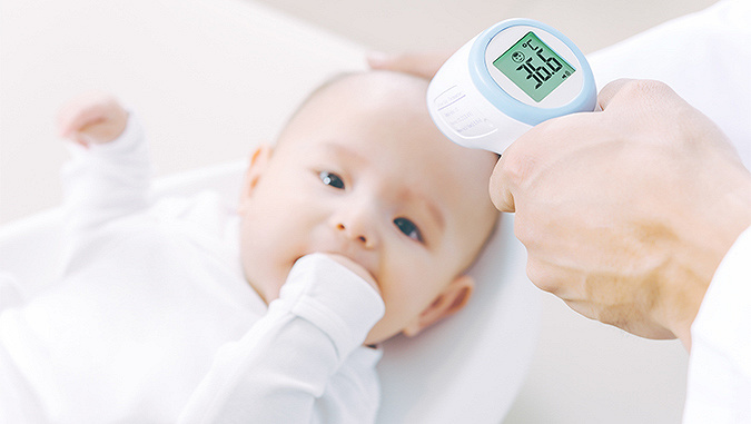 Il neonato so trova dal dottore e tiene la mano in bocca. Il medico gli misura la febbre con un termometro senza contatto - è 36,6° C.
