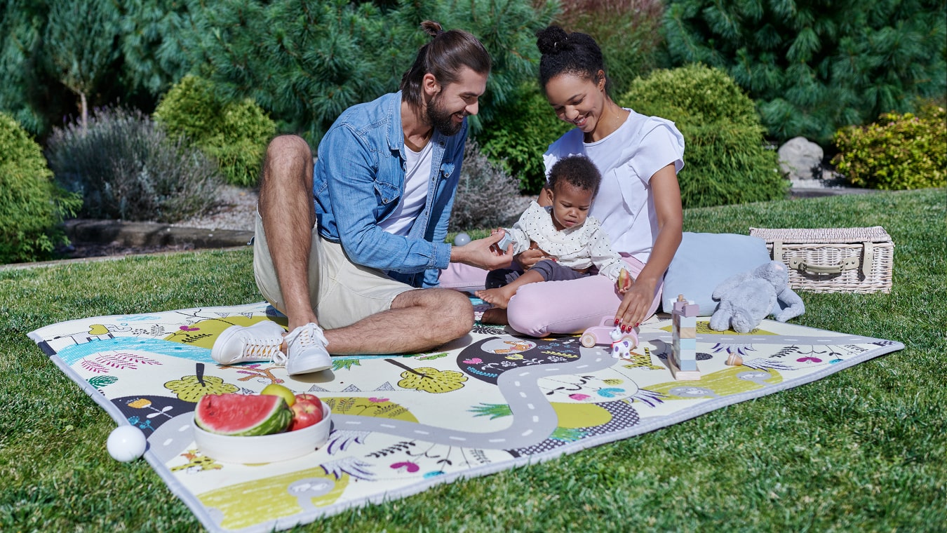 In giardino, la mamma e il papà stanno seduti e giocano con il bambino sul tappetino educativo MATTY.