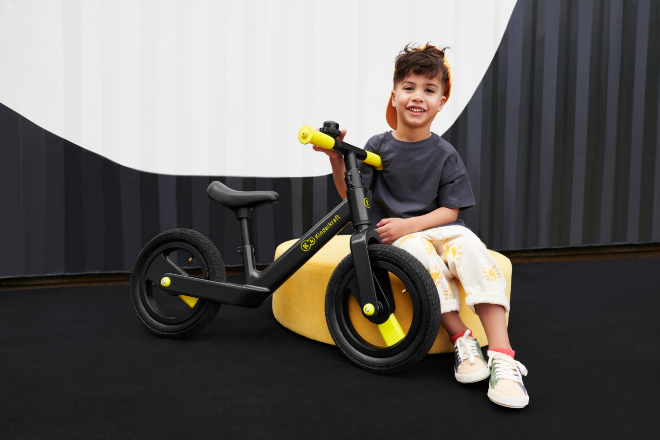 Un bambino rilassato si siede su un pouf in uno spazio astratto e afferra la bicicletta senza pedali nera