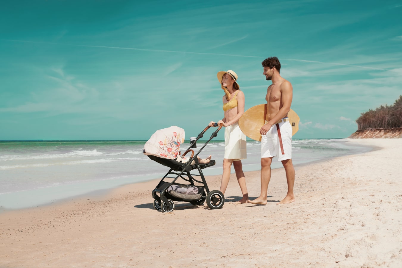 Mamma e papà stanno passeggiando sulla spiaggia con un bambino sdraiato sul passeggino nero con la cappottina beige