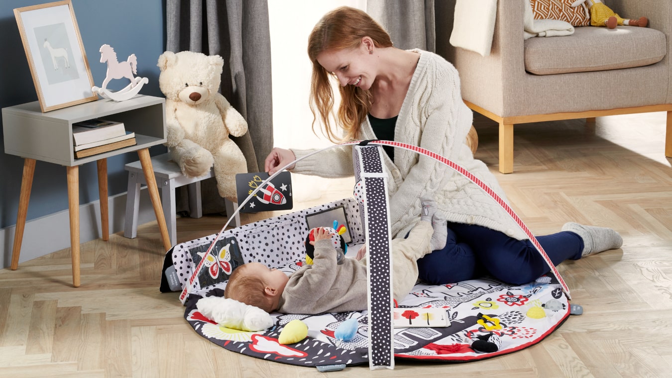 A casa, la mamma gioca felicemente con il suo bambino sdraiato sul tappetino sensoriale colorato, mostrandogli un'immagine a contrasto