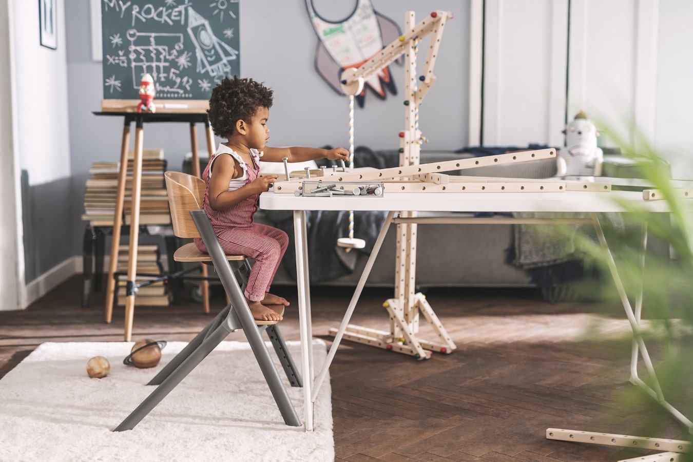 Un ragazzino con i capelli neri sta costruendo una struttura di legno, è molto concentrato, e sta seduto su una sedia LIVY Kinderkraft