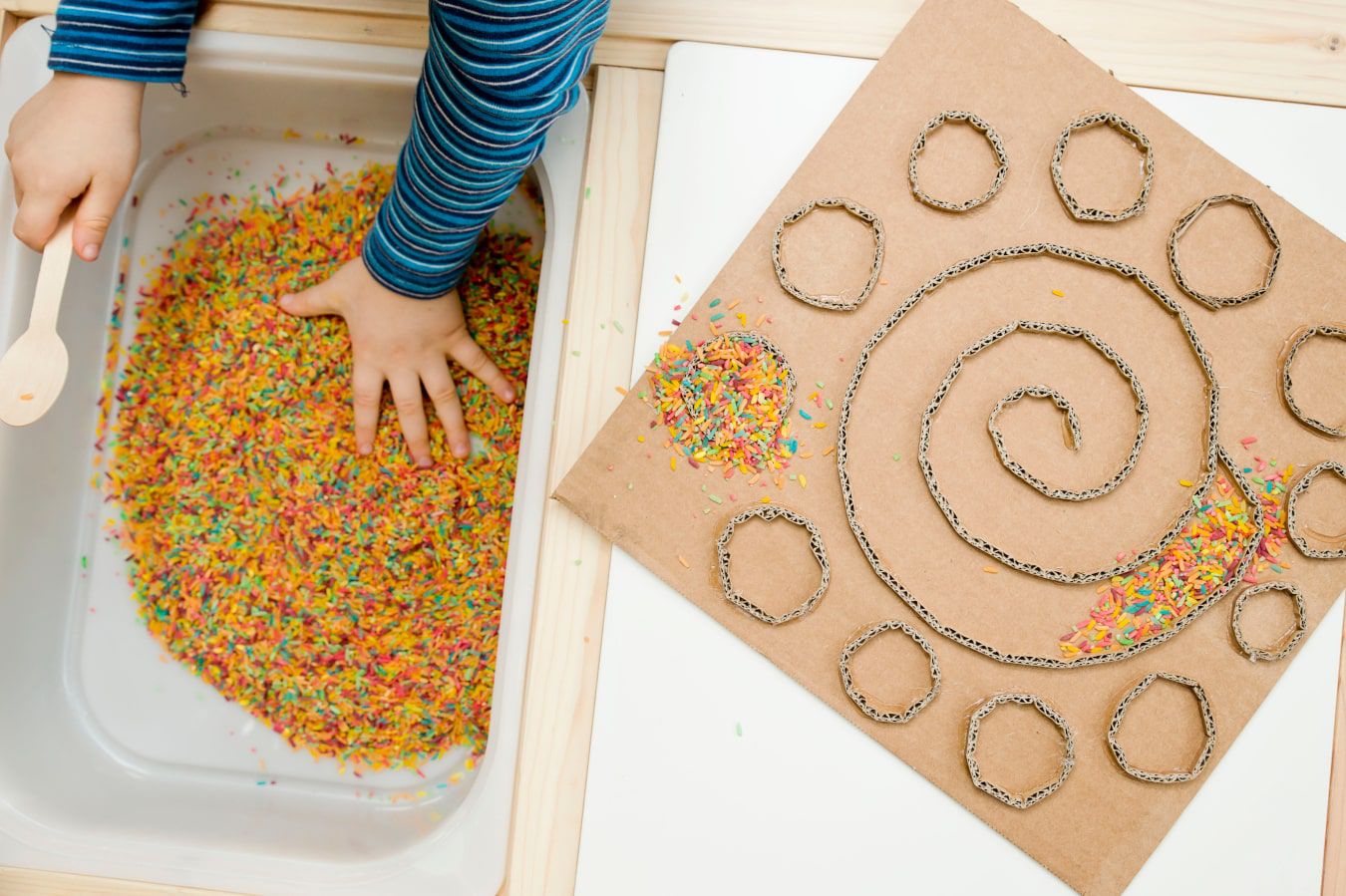 Le mani del bambino imparano a conoscere una nuova superficie – caramelle colorate e granellini di decorazioni, accanto c’è un labirinto fai da te di cartone