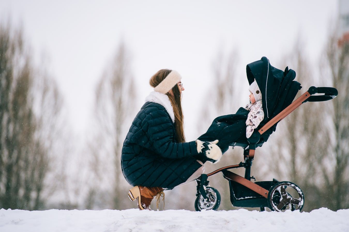 È inverno, la mamma si china verso il bambino sdraiato nel passeggino. C’è molta neve, tutti indossano le giacche